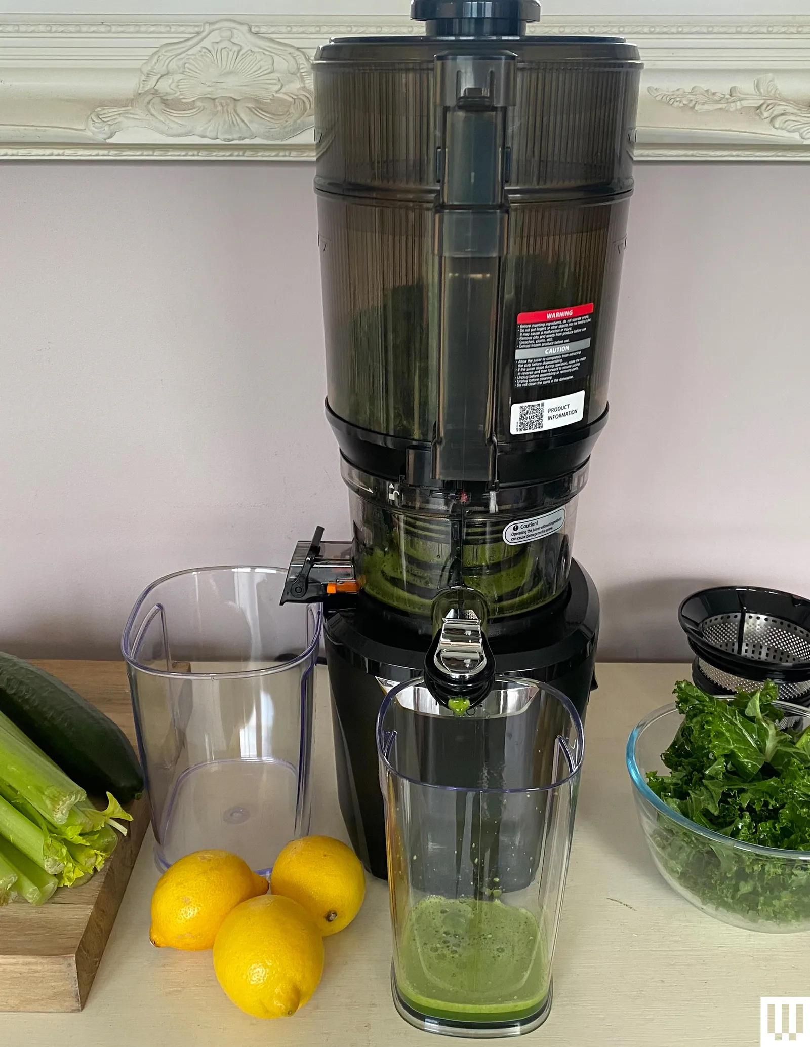 Kuvings AUTO 10 Plus HandsFree Slow Juicer a cylindrical appliance with two containers beside it's spouts sitting on a...