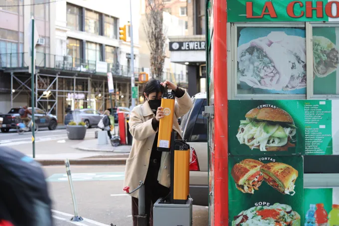 A woman swaps a battery at a food cart on a city street.