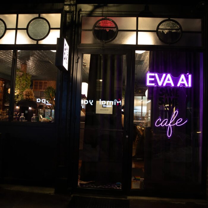 Outside view of a wine bar where you can see people through the window. In neon purple lights is the word EVA AI cafe.