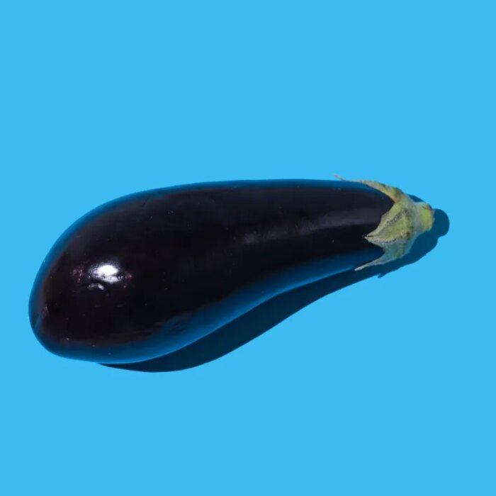 Raw eggplant with hard shadow on blue background.