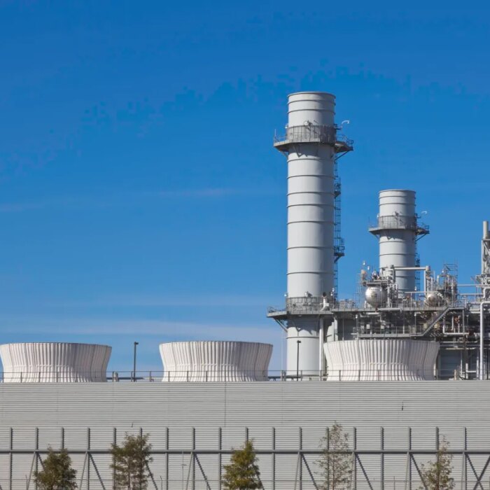 Smoke stacks from a natural gas power plant stand against a blue sky.