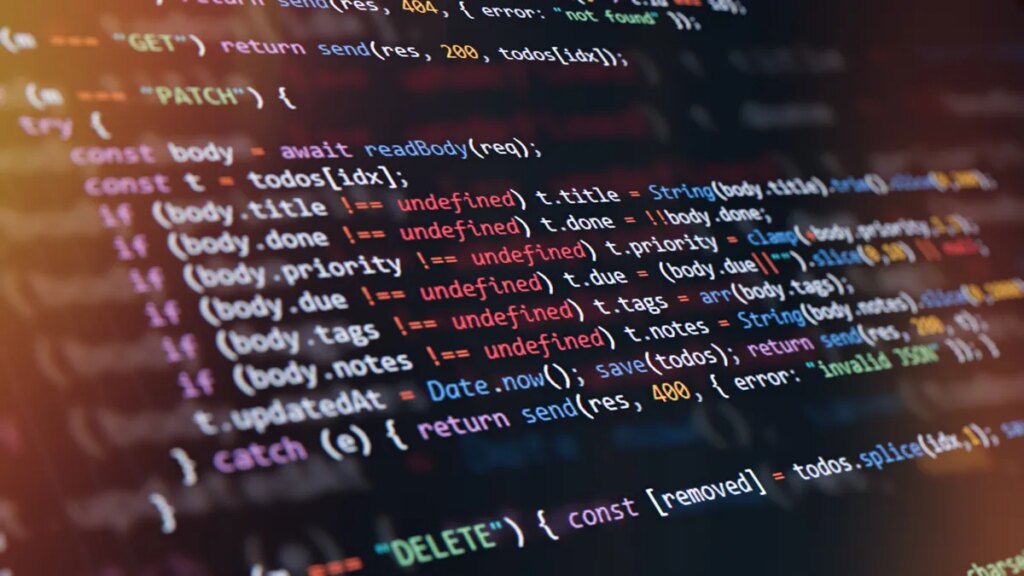 Close-up of computer screen showing colorful programming code lines with syntax highlighting and blurred light reflections.