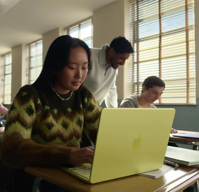 young woman seated at a classroom desk using a MacBook Neo