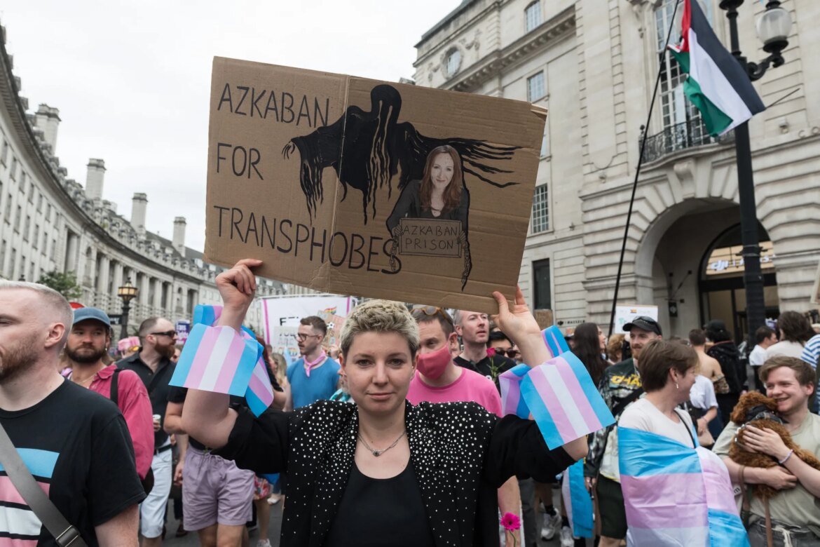 A person holding up a cardboard sign depicting author JK Rowling and a shadowy hooded figure. The sign reads: Azkaban for transphobes.