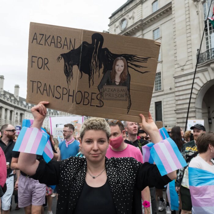 A person holding up a cardboard sign depicting author JK Rowling and a shadowy hooded figure. The sign reads: Azkaban for transphobes.