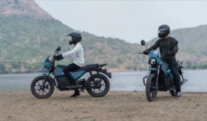 Two motorbikes with riders are parked in front of a lake.