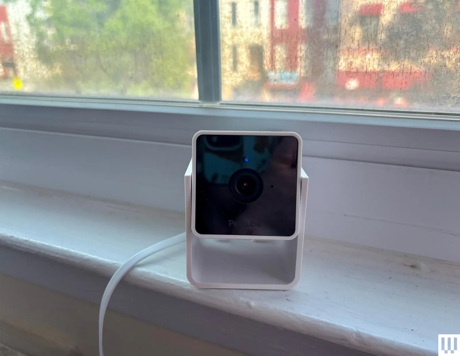 Square white pet camera with black screen sits on a white window sill.
