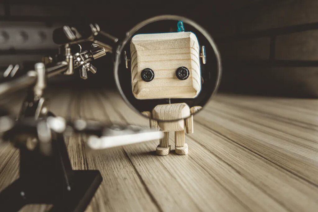 Wooden Robot Android Stands On A Table Under A Magnifying Glass. Metal Clamps With Magnifying Glass