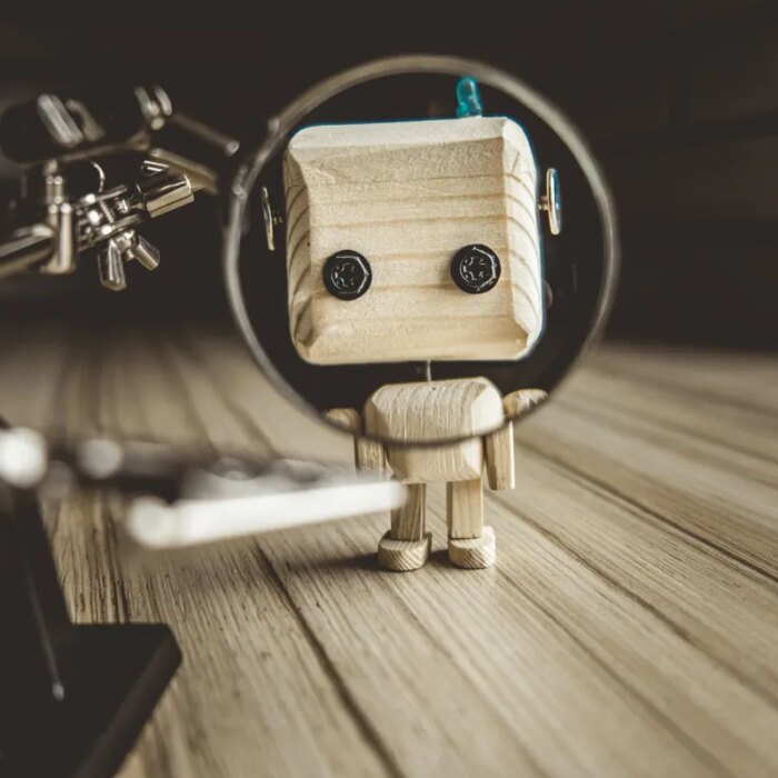 Wooden Robot Android Stands On A Table Under A Magnifying Glass. Metal Clamps With Magnifying Glass