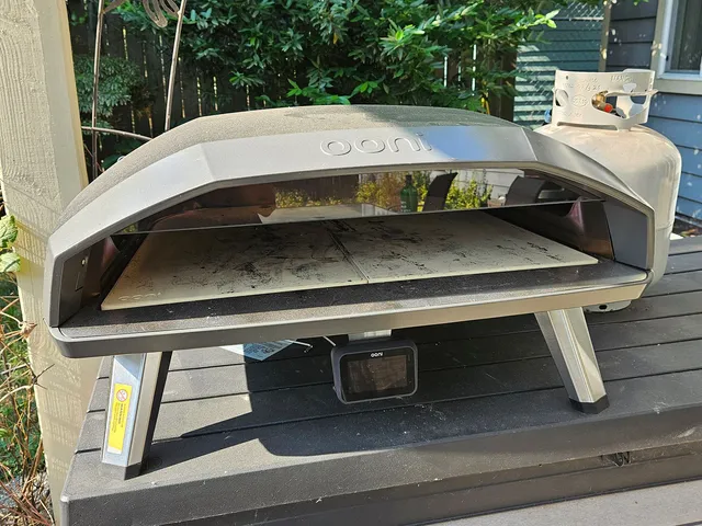 Ooni Koda 2 Max, a pizza oven with legs and angular top, sitting on a surface outdoors beside a house