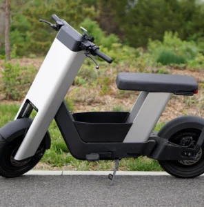 A photo of a silver e-bike from the side, in front of trees.