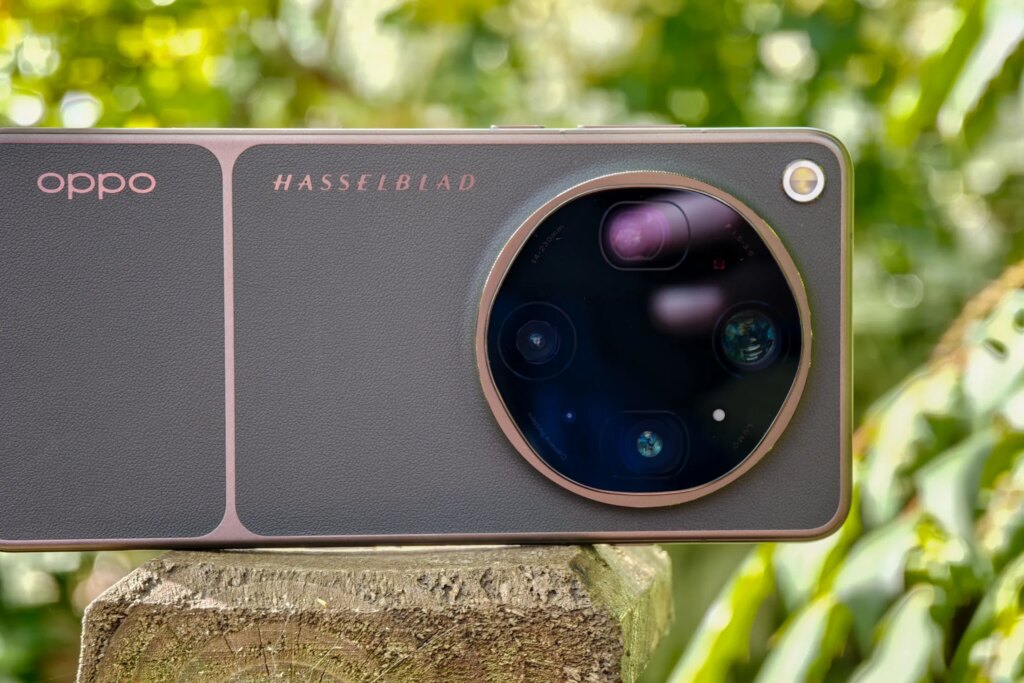 Photo of Oppo Find X9 Ultra resting horizontally on a wooden post in front of green plants, showing the rear cameras