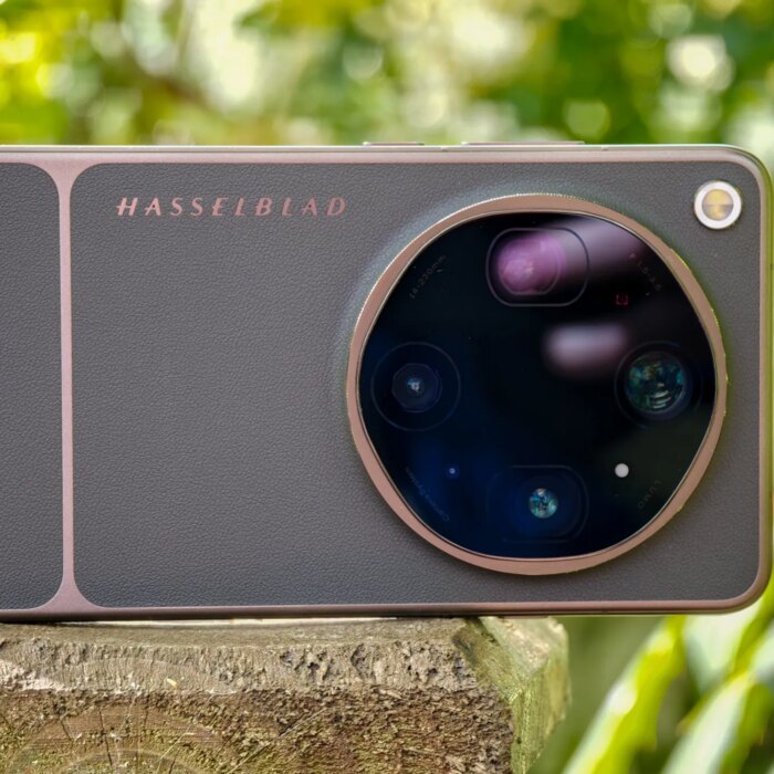Photo of Oppo Find X9 Ultra resting horizontally on a wooden post in front of green plants, showing the rear cameras