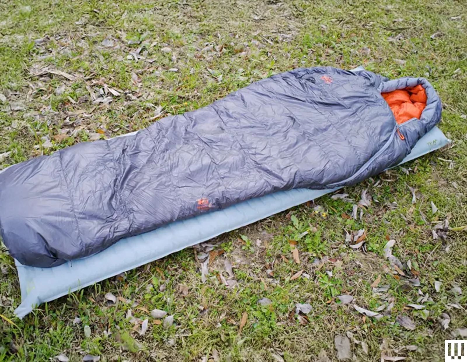 Grey sleeping bag on top of light blue inflatable sleeping pad both laying in the grass