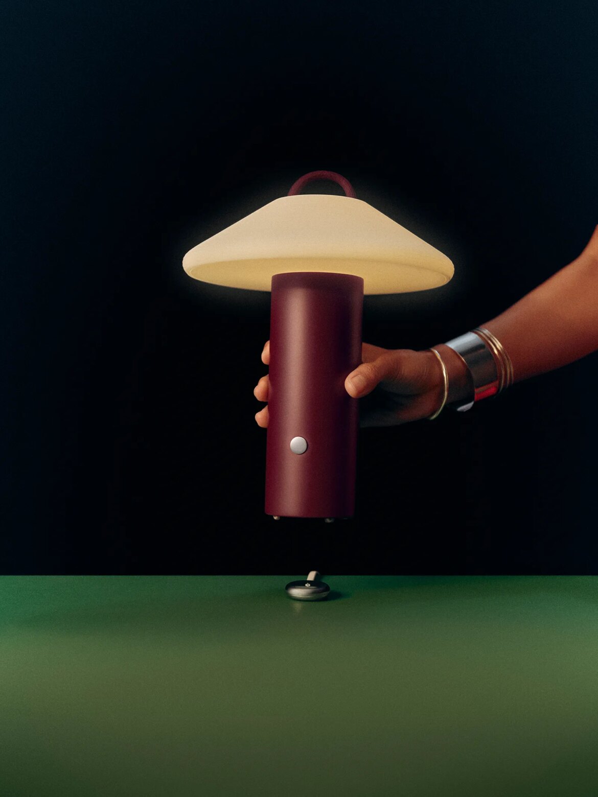 A person sets a dark red lamp onto a table