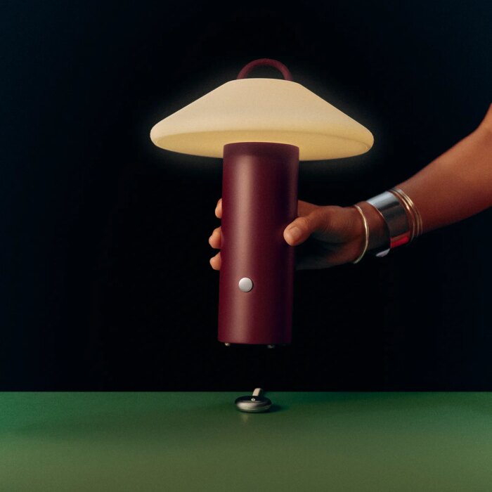A person sets a dark red lamp onto a table