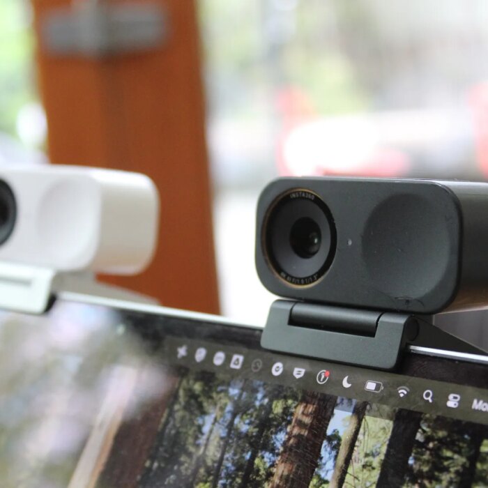 Two small rectangular webcams clipped to the top of a laptop screen one in white and the other black
