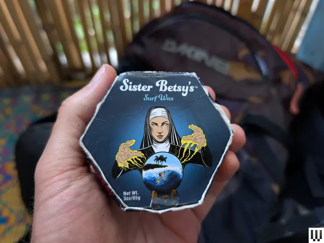 Hand holding a hexagonal shaped container of surfboard wax
