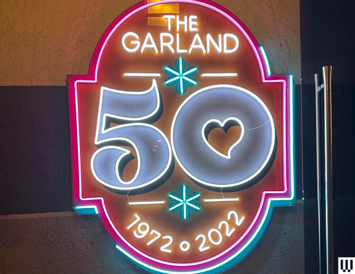 Neon sign in pink yellow teal and white that says The Garland 50 1972 to 2022