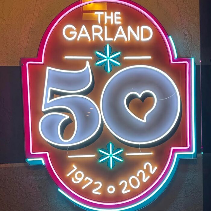Neon sign in pink yellow teal and white that says The Garland 50 1972 to 2022