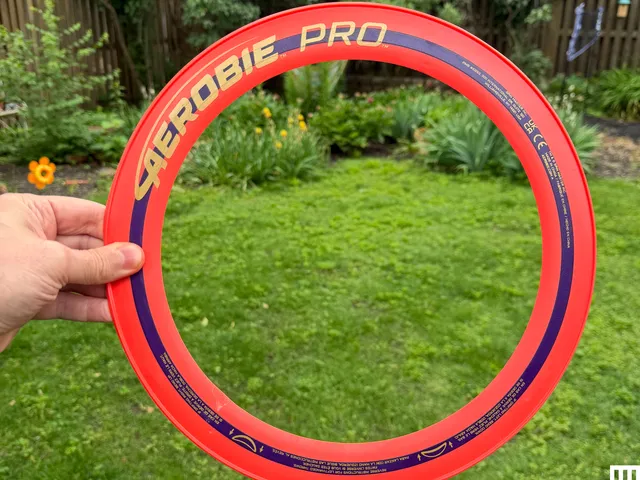 Hand holding a bright red thin ring with a backyard in the distance