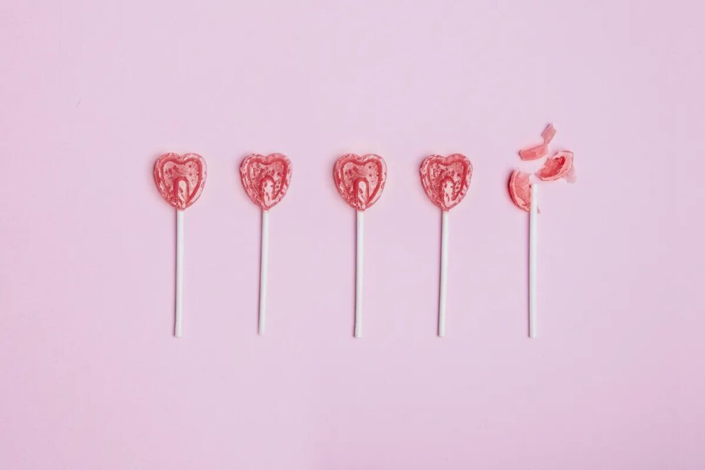 Five lollipop hearts on a pink floor, but the last one is smashed to pieces.