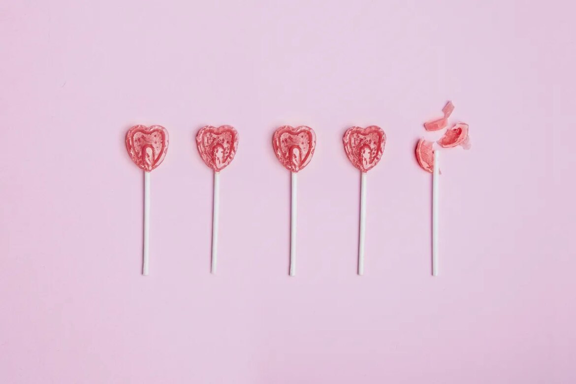 Five lollipop hearts on a pink floor, but the last one is smashed to pieces.