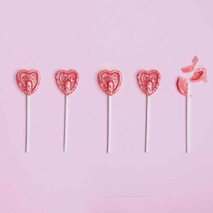 Five lollipop hearts on a pink floor, but the last one is smashed to pieces.