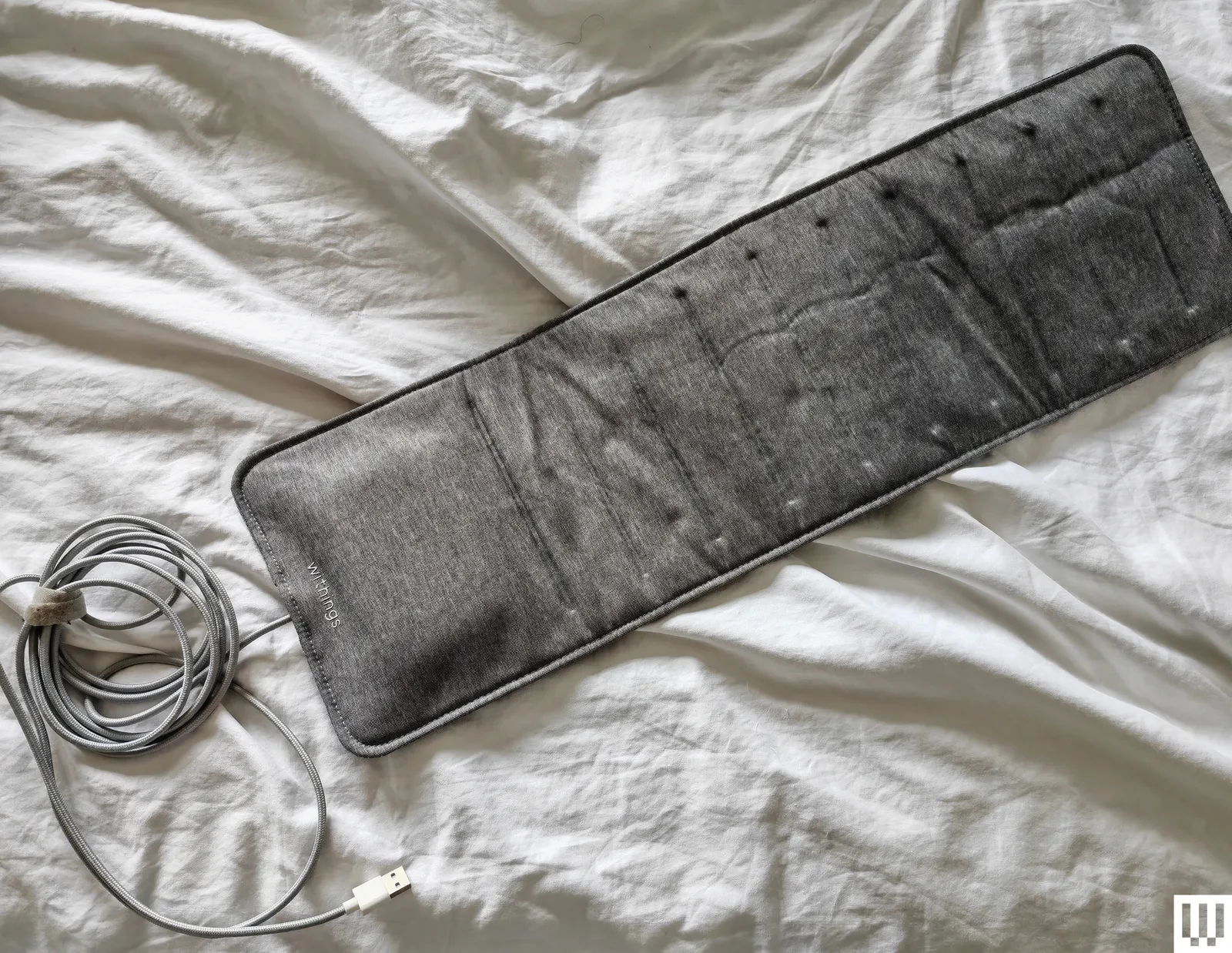 Overhead view of the Withings Sleep Tracking Mat a flat rectangular pad with a cord coming out of one end on top of a...