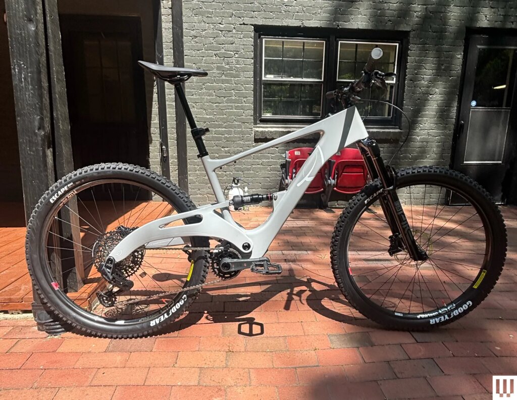 Side view of a black and white electric mountain bike parked on a paved sidewalk with a grey residential building in the...