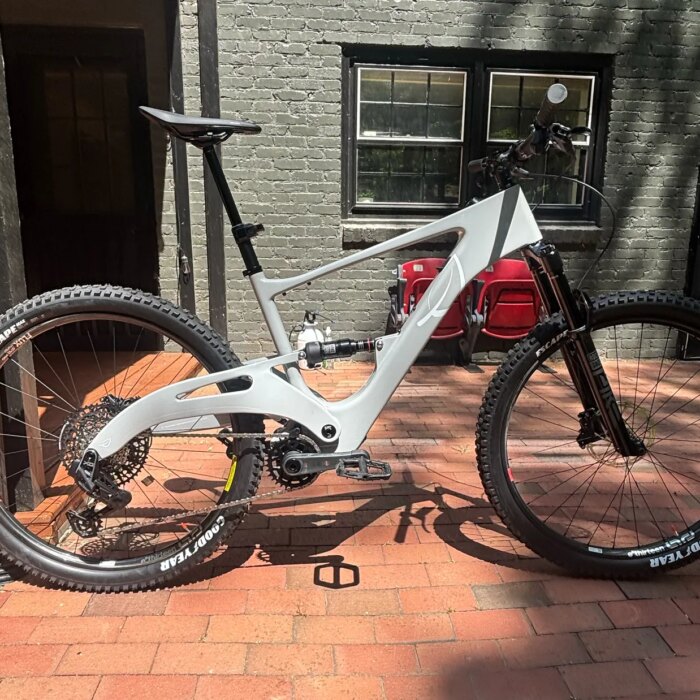 Side view of a black and white electric mountain bike parked on a paved sidewalk with a grey residential building in the...