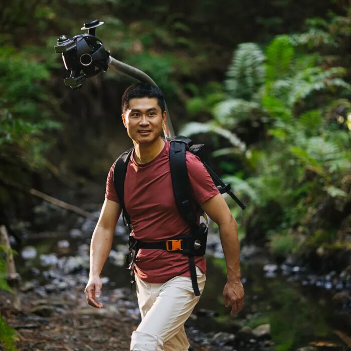 Man hiking in a forest wearing Odyssey camera pack