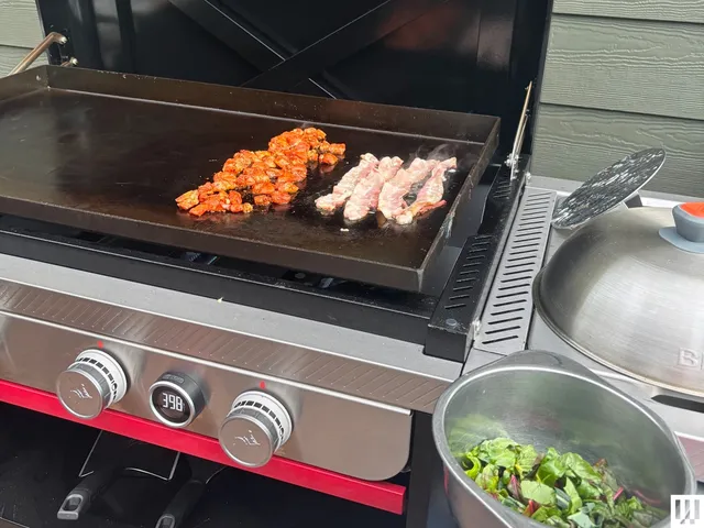 Closeup of a black griddle with silver knobs as food cooks on top