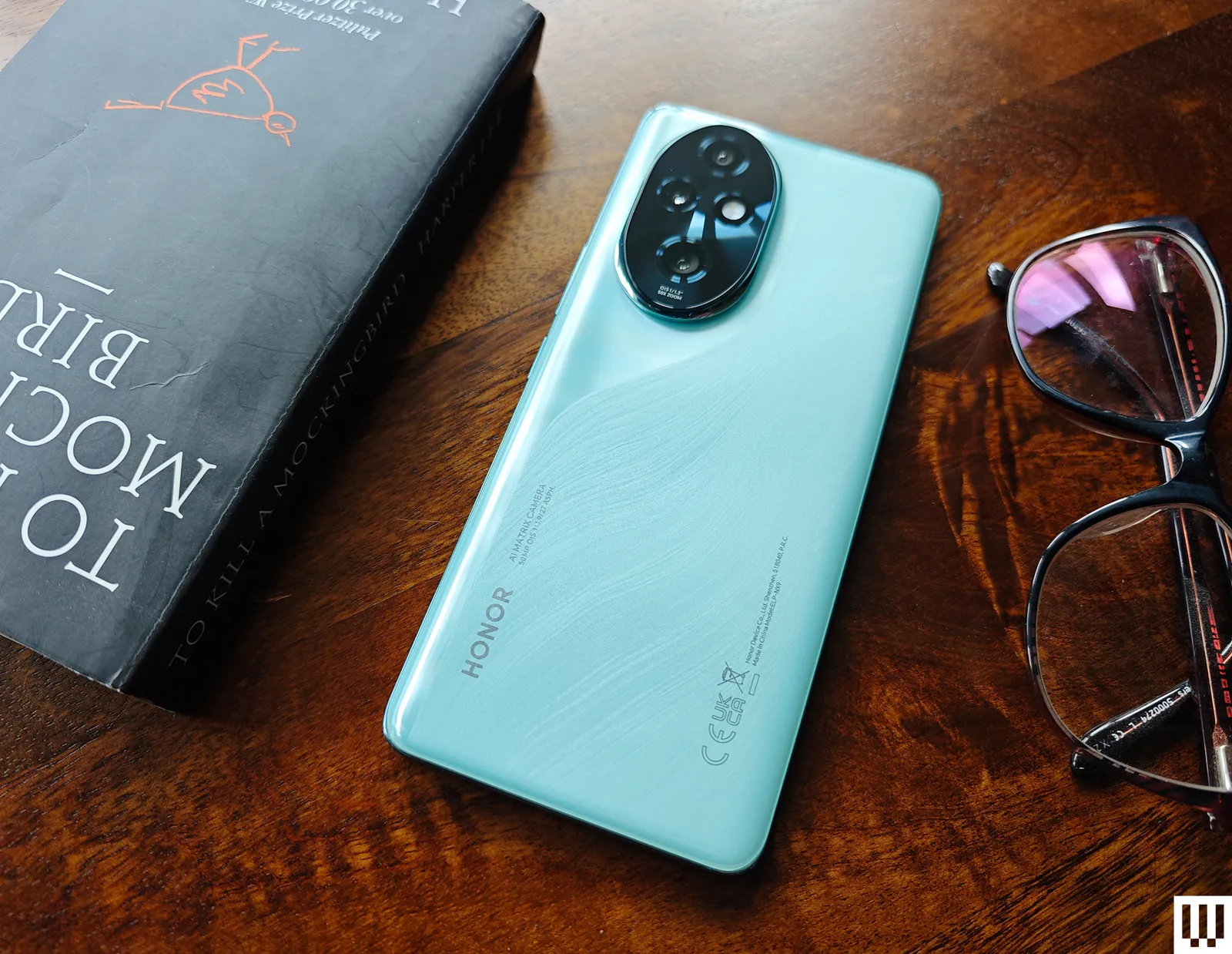 A book teal mobile phone and pair of glasses on a wooden surface