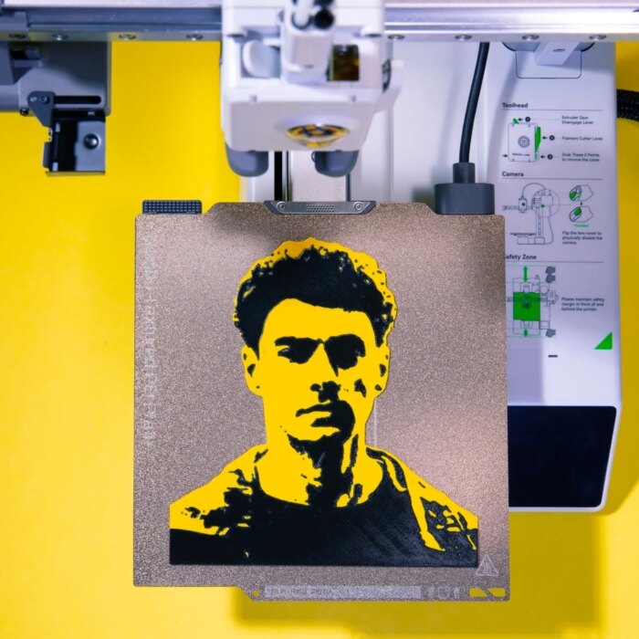 Black and yellow 3D print of Luigi Mangione sitting on a 3D print bed.